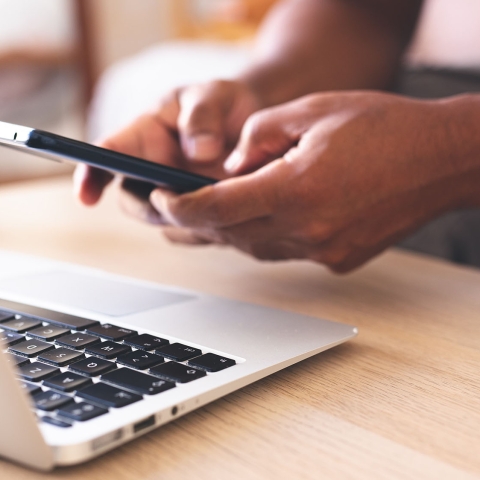 Hands on a cellphone over a laptop