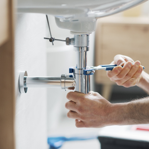A plumber working on pipes underneath a sink