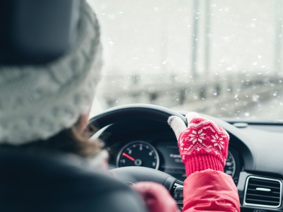 Woman in red jacket, hat, and gloves driving on highway during winter snowfall