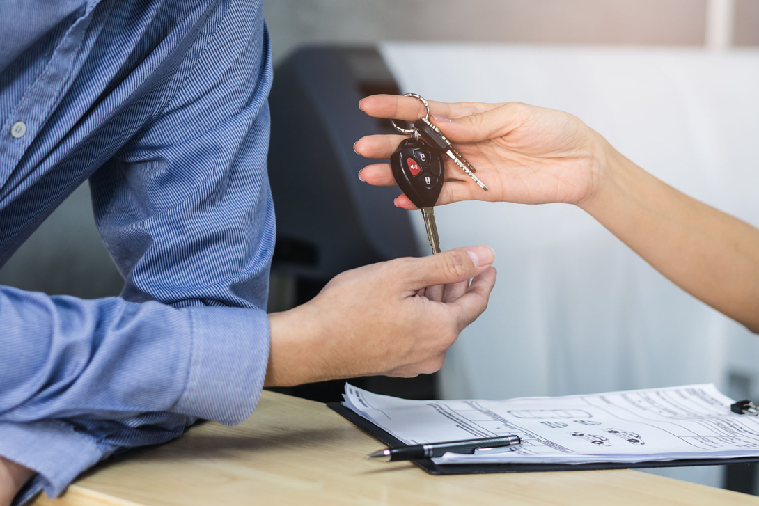 Close up view hands of agent giving car key to client renting a vehicle in rental office